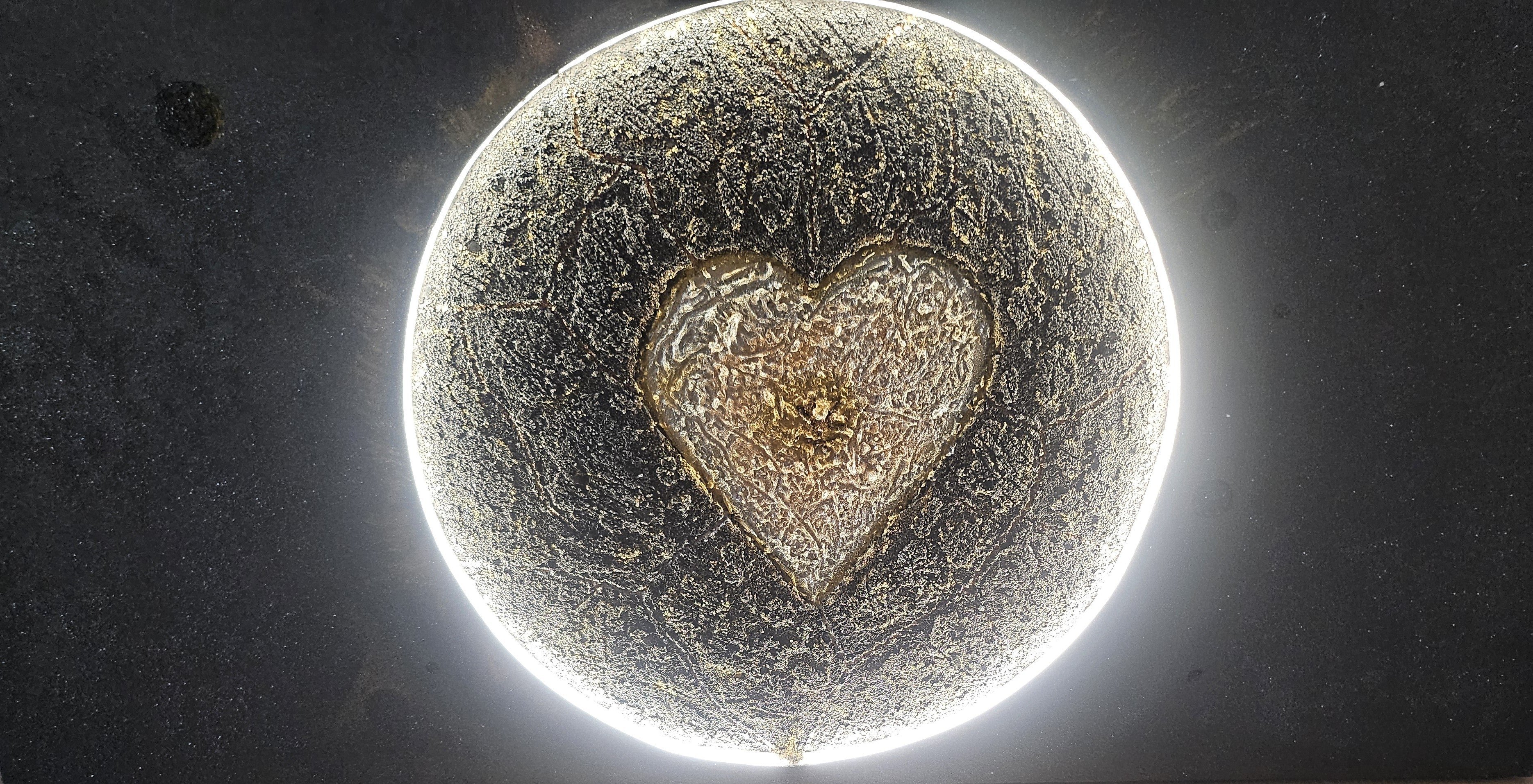 Close-up of Genesis, an illuminated handcrafted relief artwork by Project X. A glowing golden heart emerges from the center of a planet, symbolizing the source of life and the flow of love through the universe.