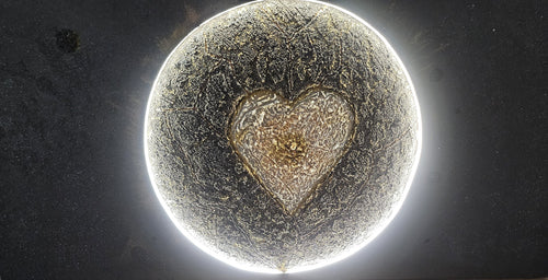 Close-up of Genesis, an illuminated handcrafted relief artwork by Project X. A glowing golden heart emerges from the center of a planet, symbolizing the source of life and the flow of love through the universe.
