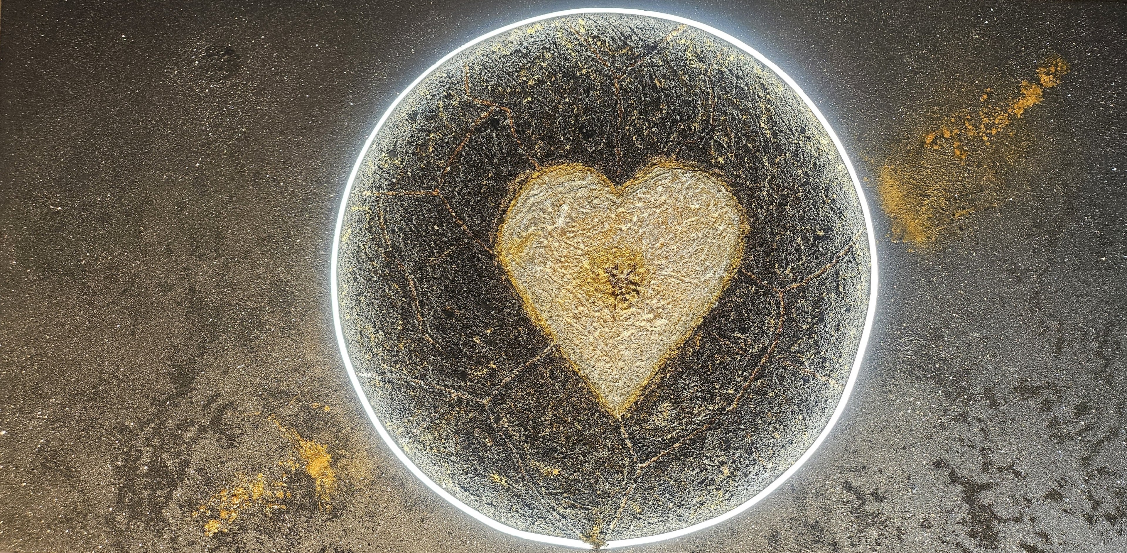 Close-up of Genesis, an illuminated handcrafted relief artwork by Project X. A glowing golden heart emerges from the center of a planet, symbolizing the source of life and the flow of love through the universe.